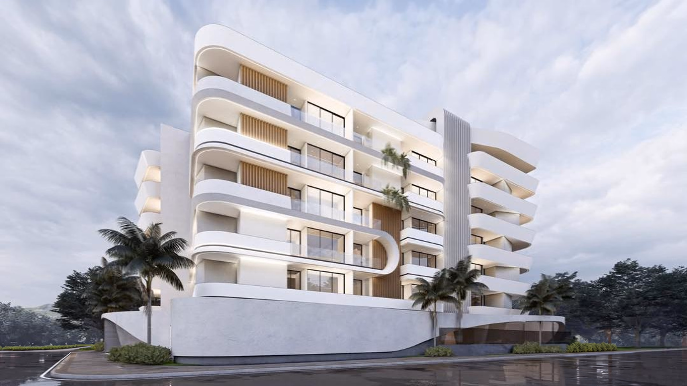 Curve under an overcast sky: a five-storey apartment building whose white balconies curve around each floor, palms along its frontage and the wet road in front of it.