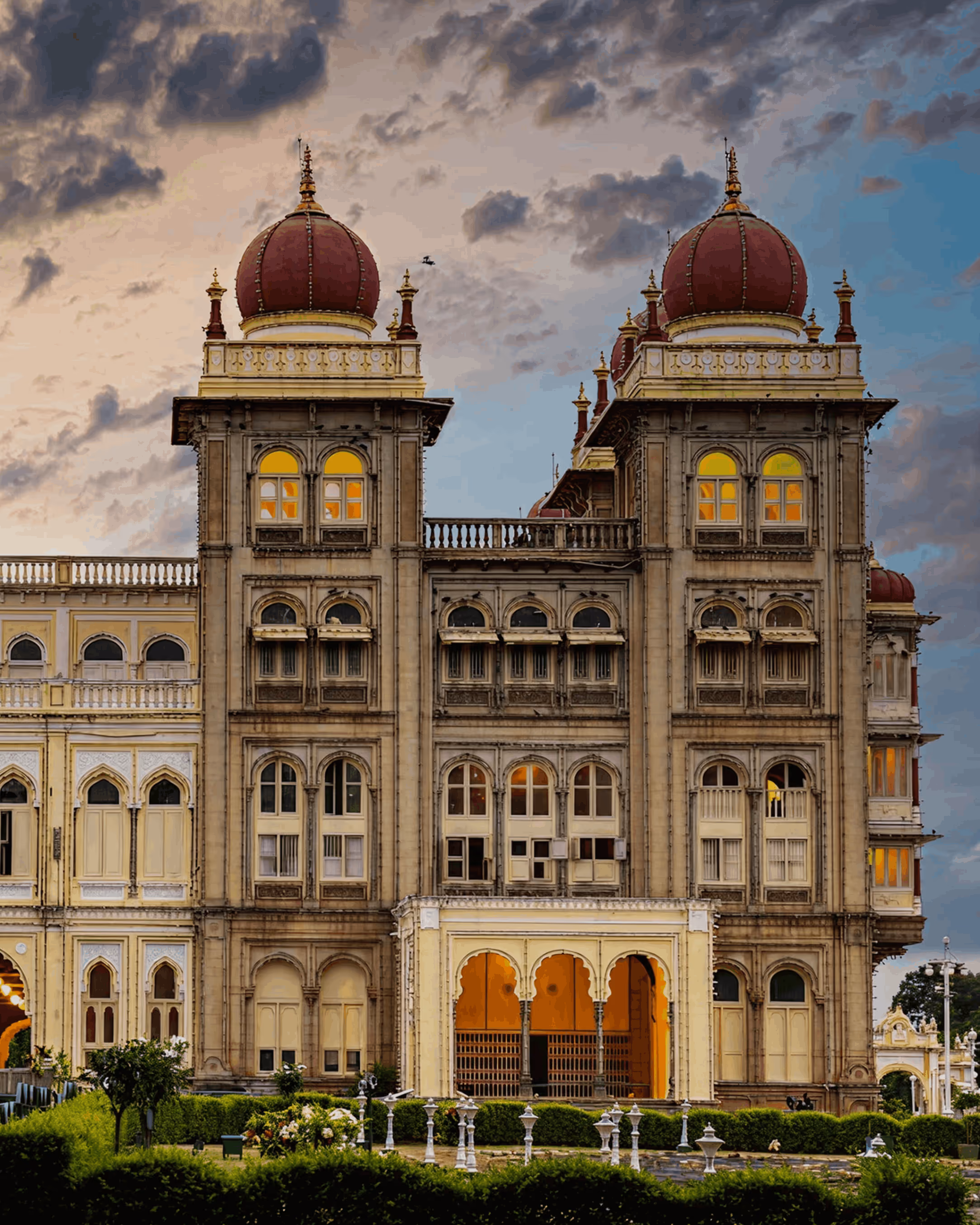 Mysore Palace at dusk, its domed towers lit against a clouded sky.